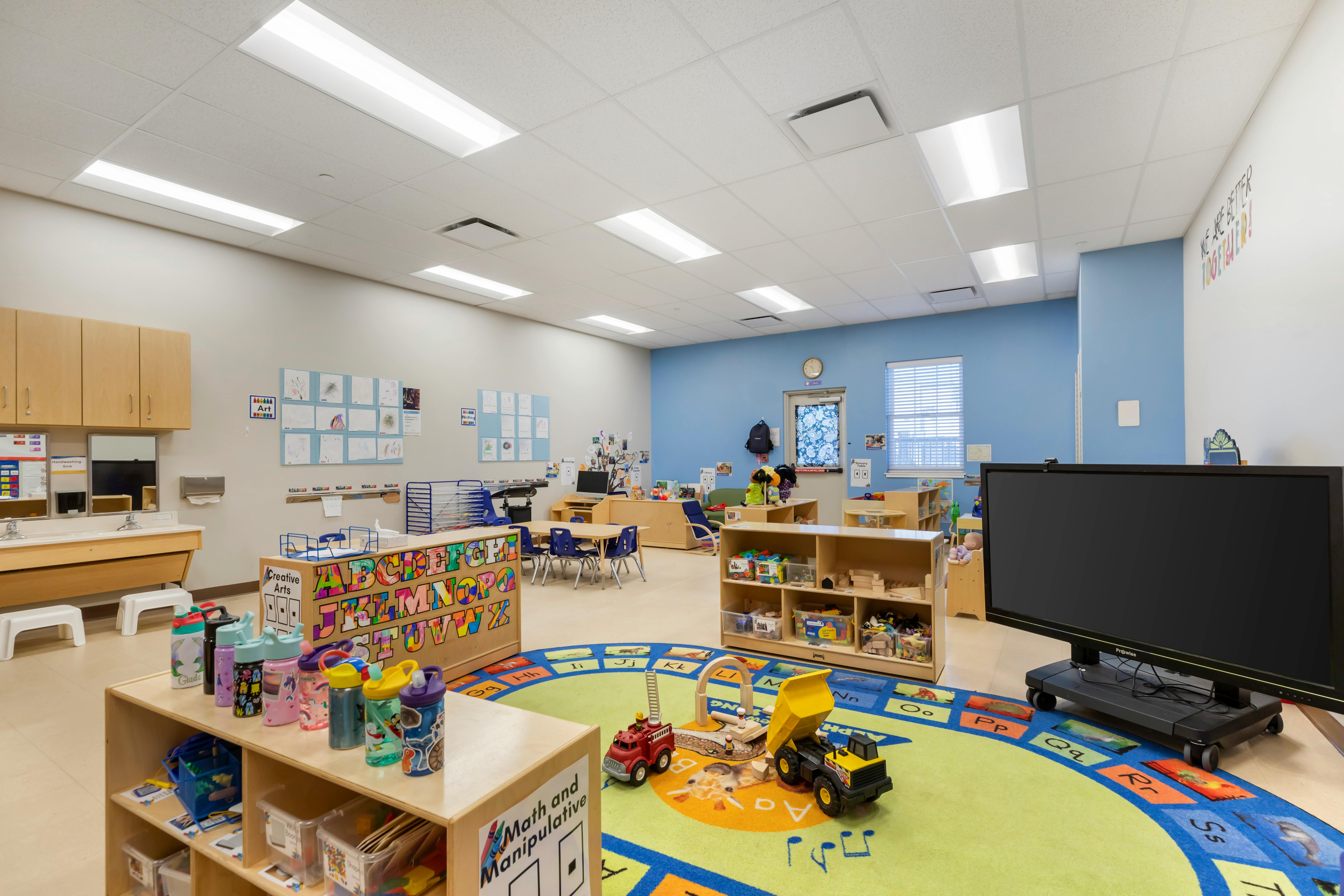 Classroom with small tables and chairs, toys on a circular rug