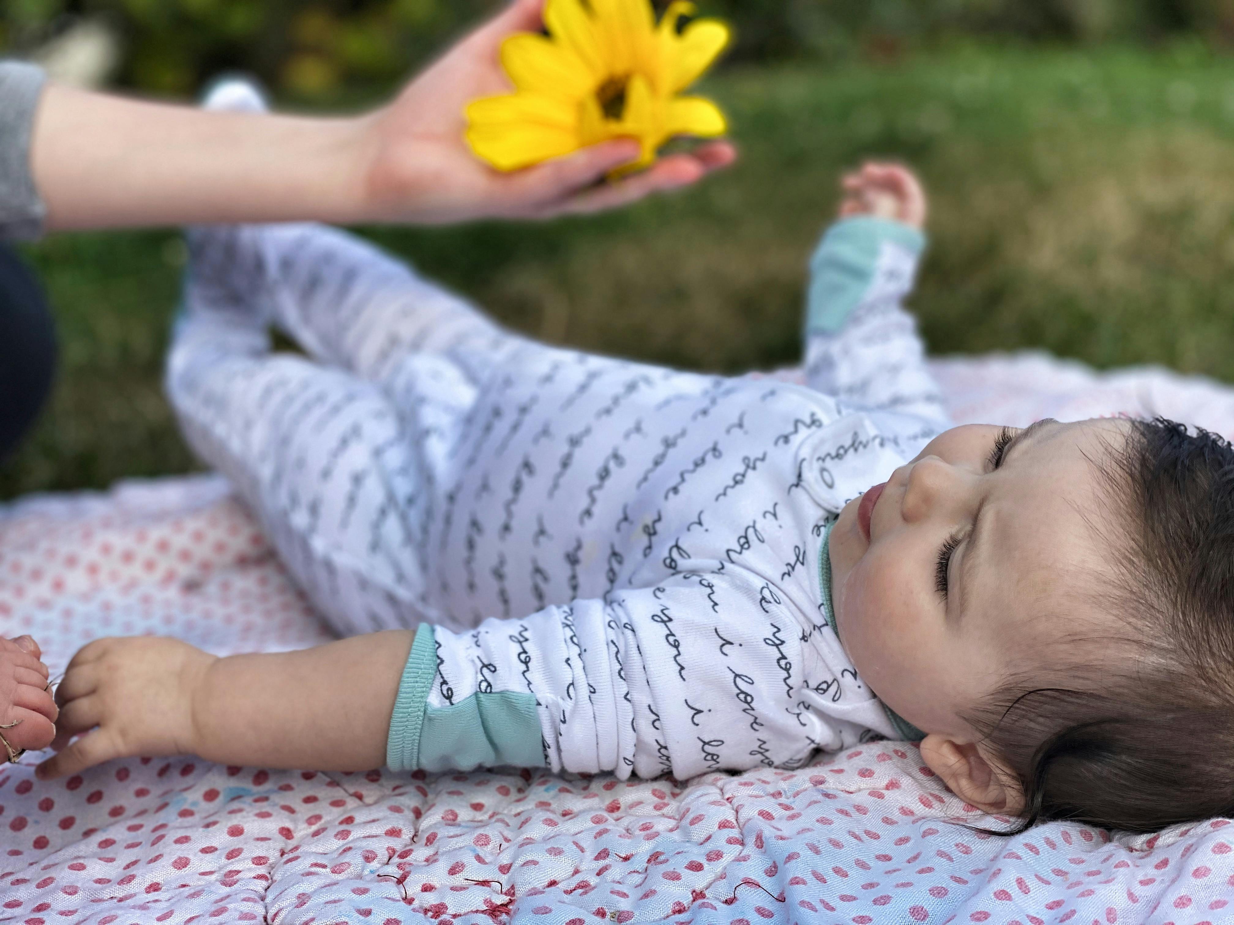 Person holding a yellow flower over a child lying on a blanket