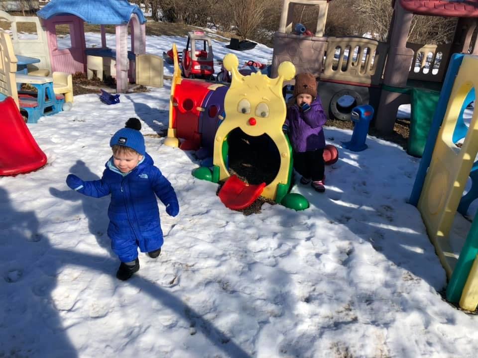 Two children playing in snow on a playground