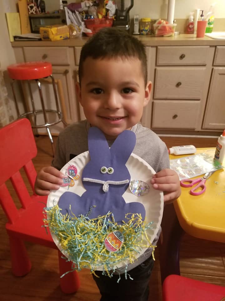 Child holding a paper plate craft with a purple bunny and colorful paper grass