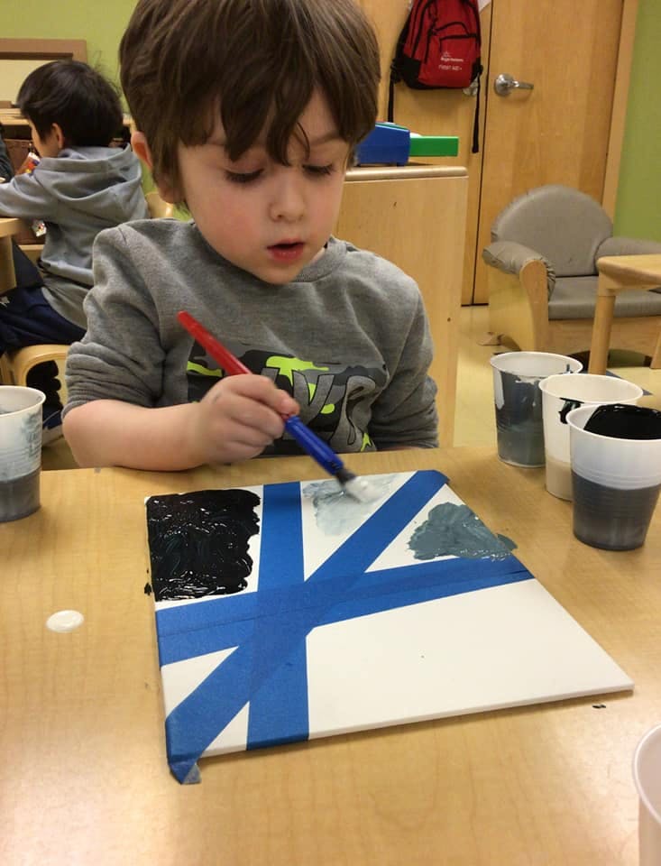 Child painting a canvas with blue tape creating a cross design
