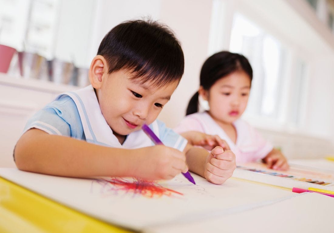 Child drawing with a purple marker, another child in the background