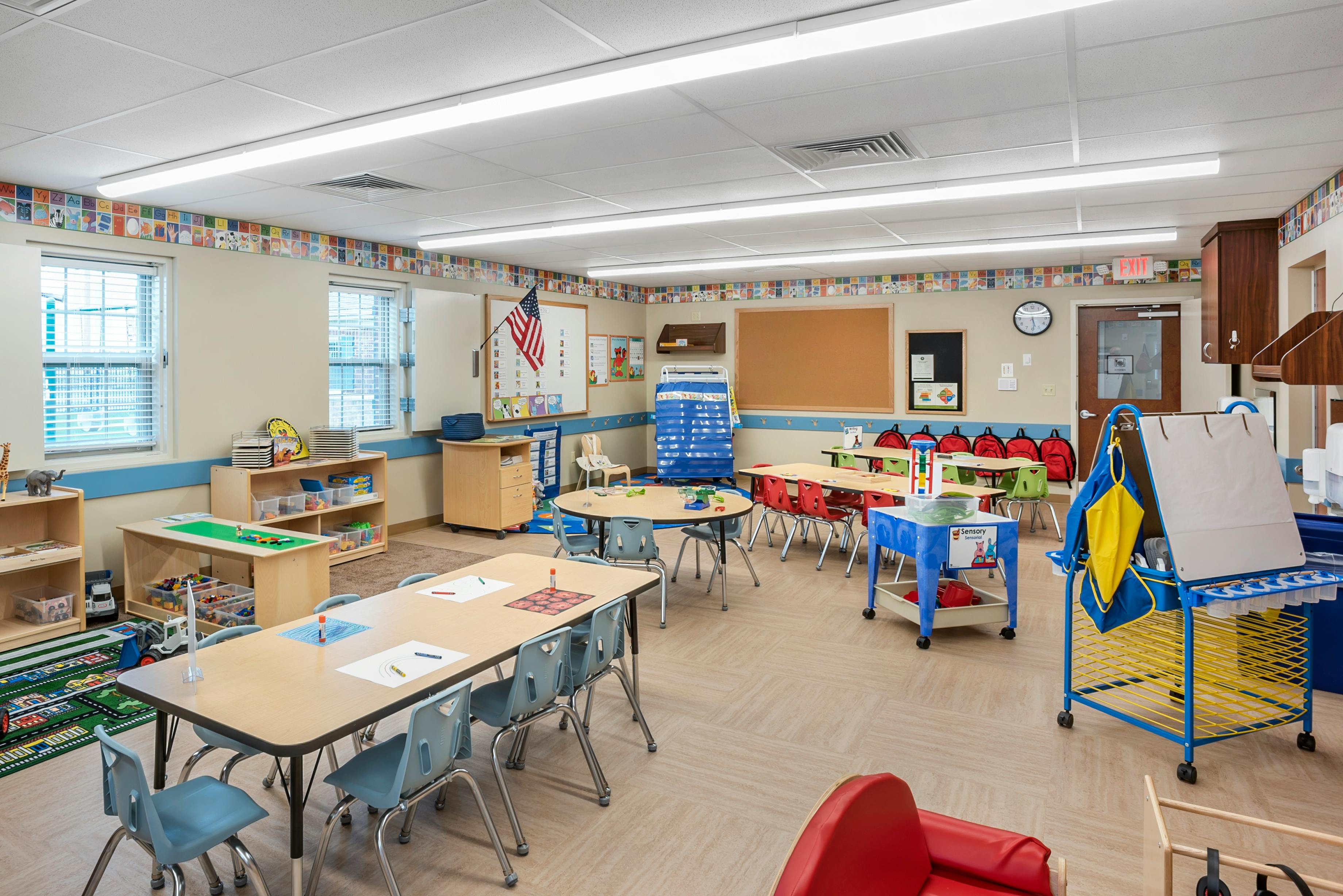 Classroom with small tables and chairs, toys, and an American flag