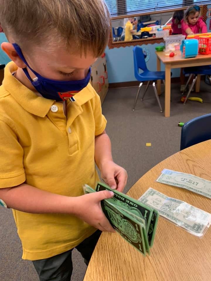 Child in a classroom holding play money