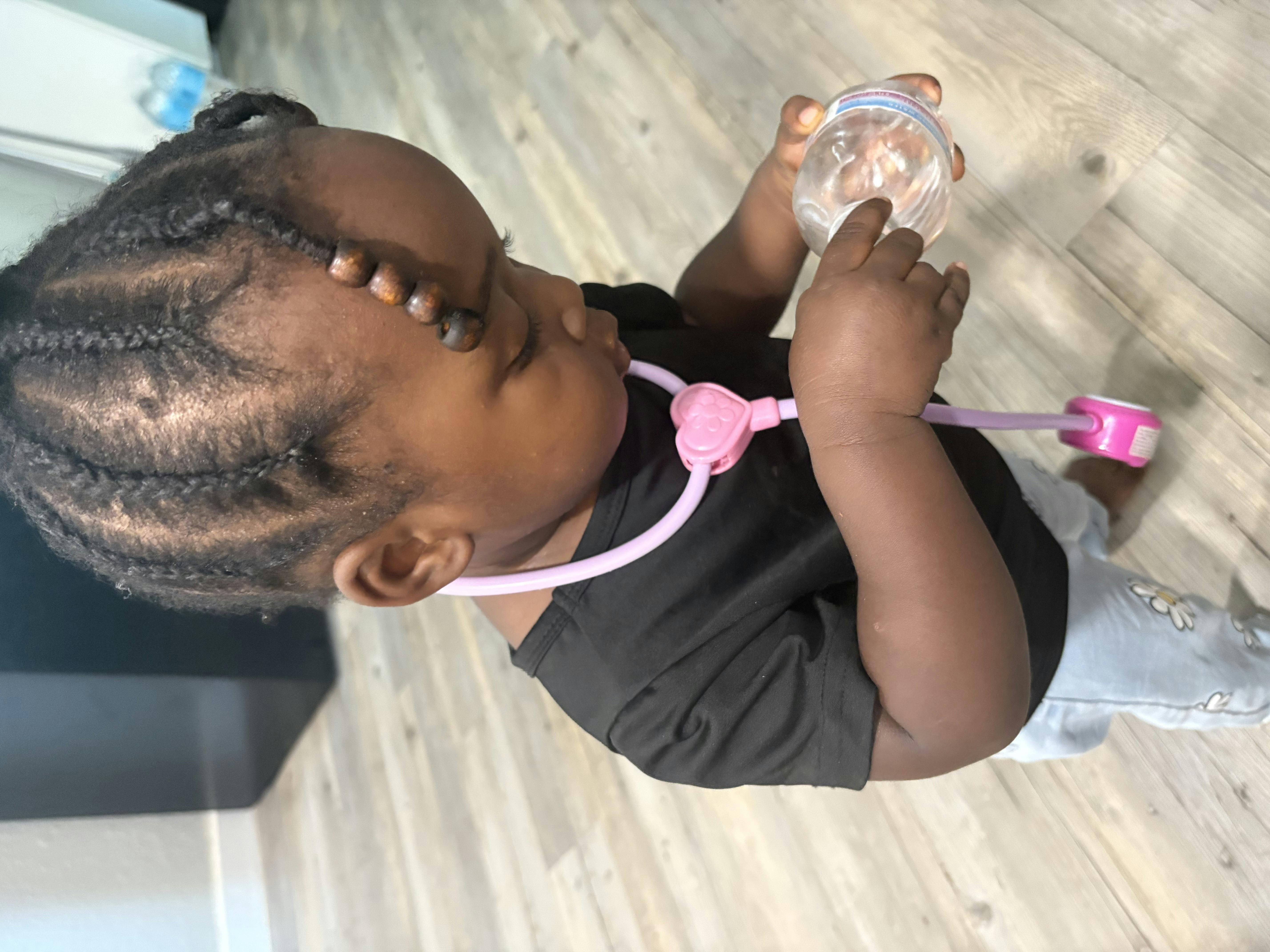 Child wearing a toy stethoscope and holding a clear cup