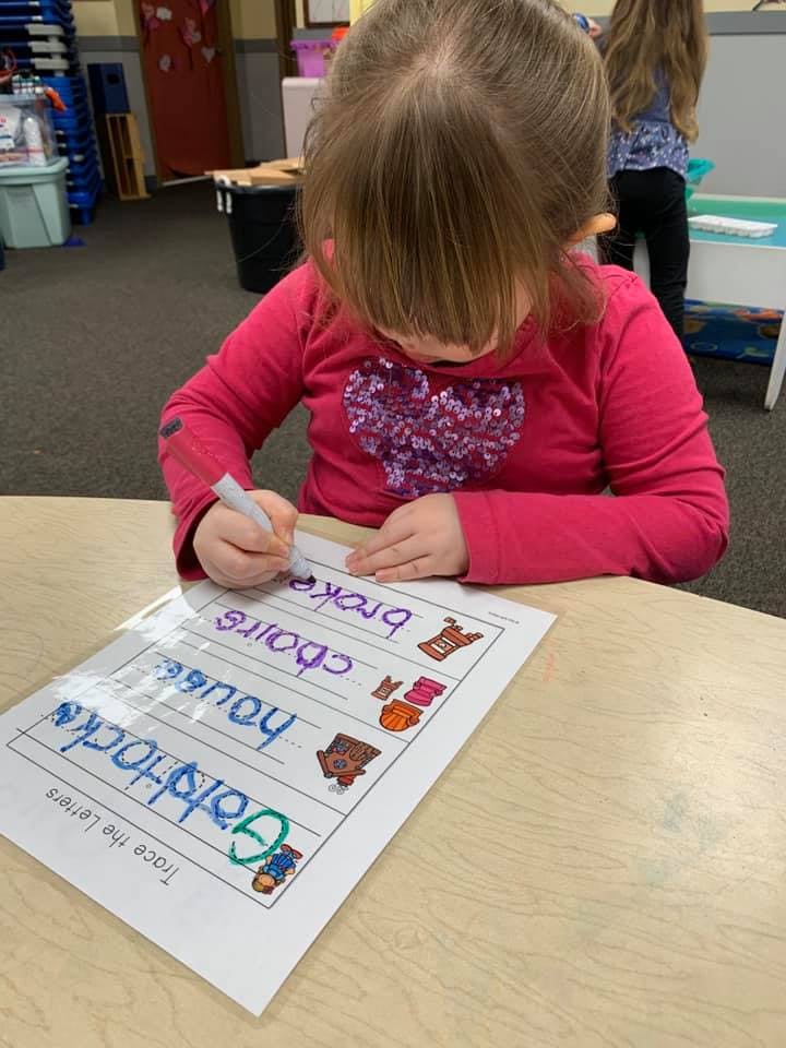 Child tracing letters on a worksheet at a table