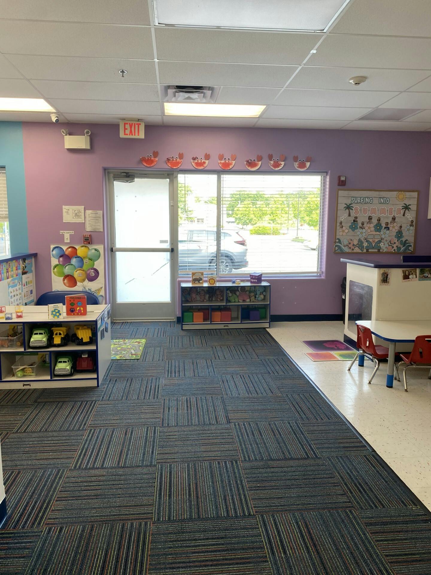 A classroom with purple walls, a patterned carpet, and a window looking outside