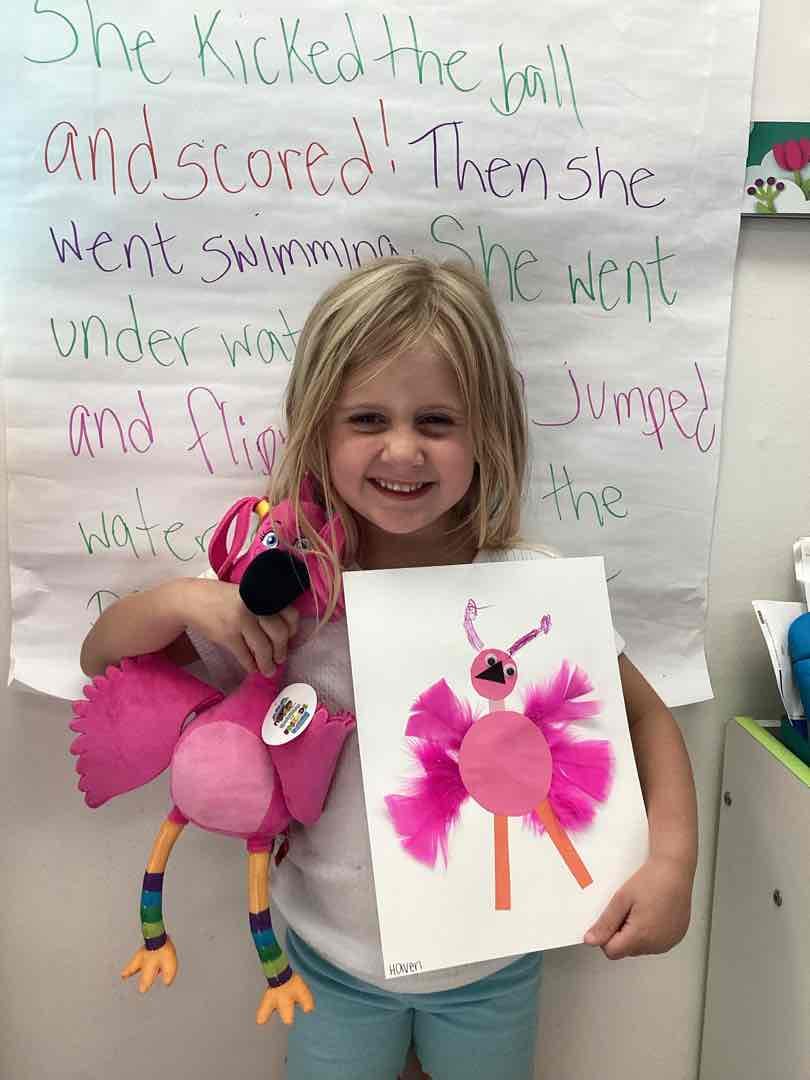 Child holding a pink flamingo toy and a drawing of a pink bird