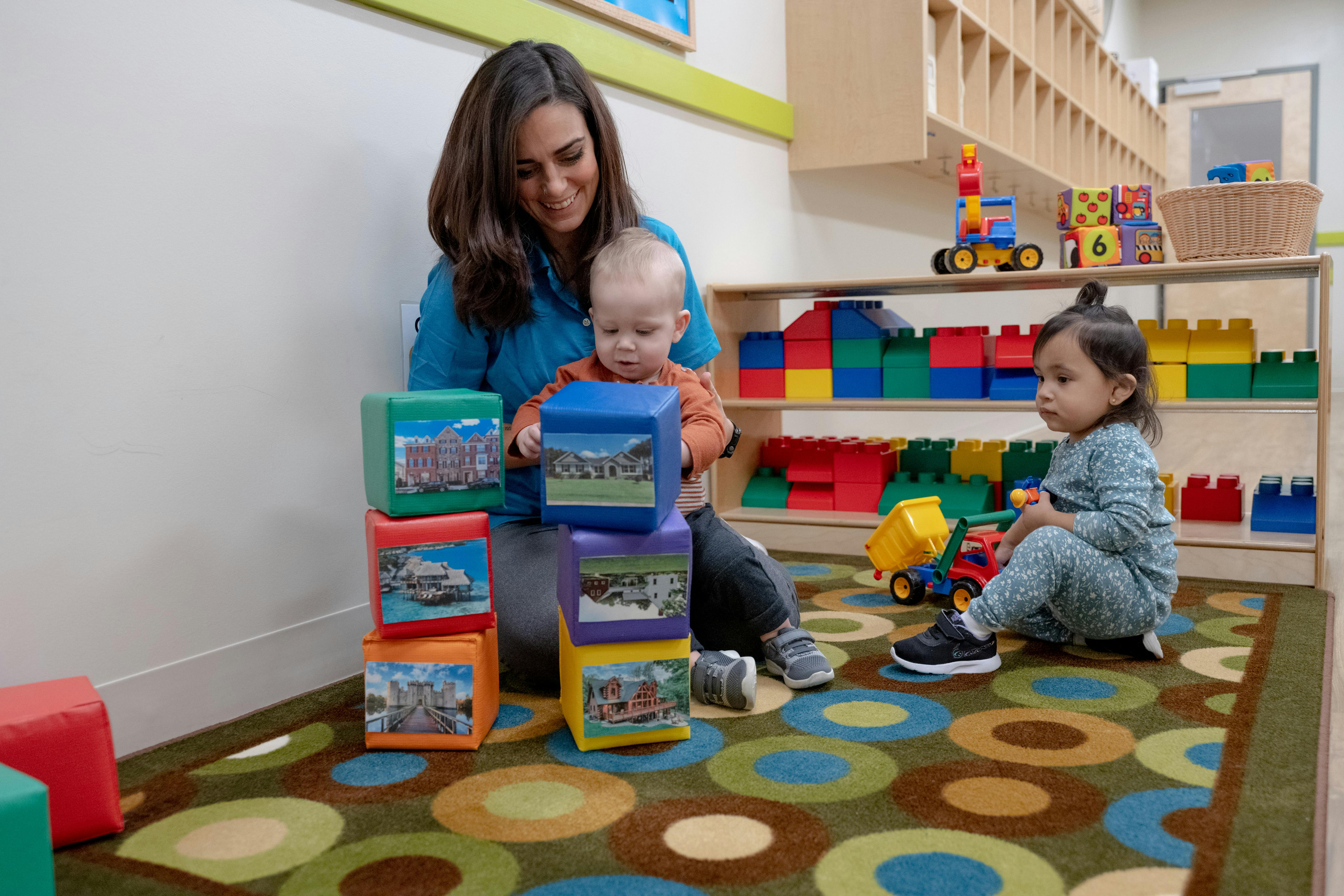 Person and two children playing with blocks in a classroom