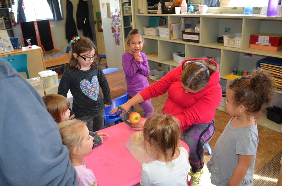 Adult and children gathered around a table with an apple