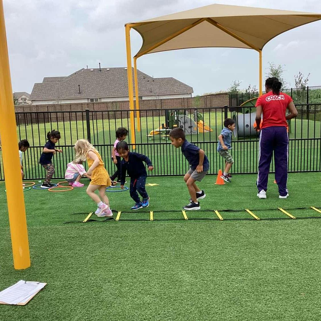 Children and an adult exercising on a green turf field