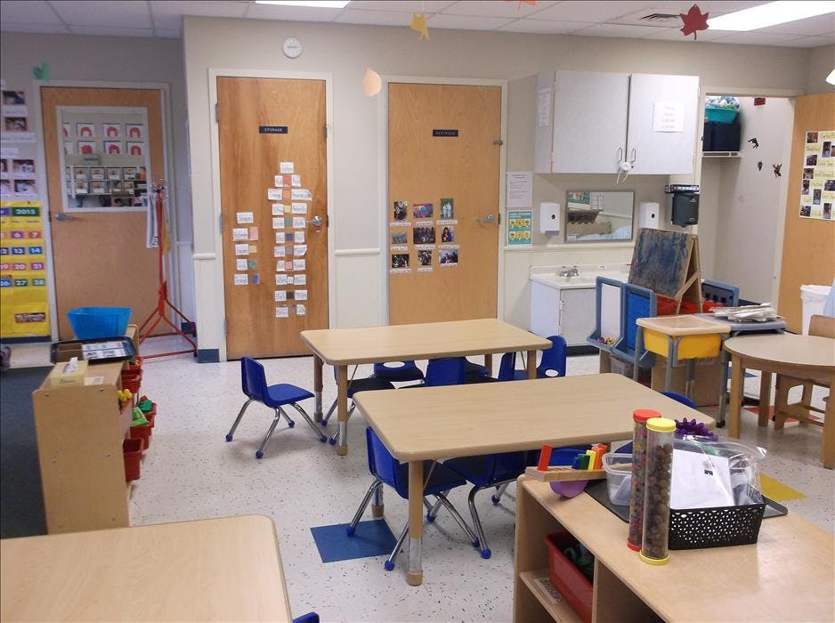 Empty classroom with small tables and chairs, two doors, and a sink area