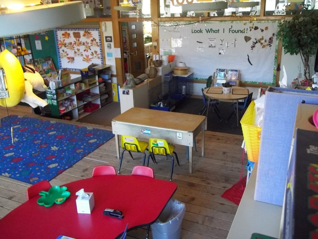 Classroom with small tables and chairs, a blue rug, and a whiteboard