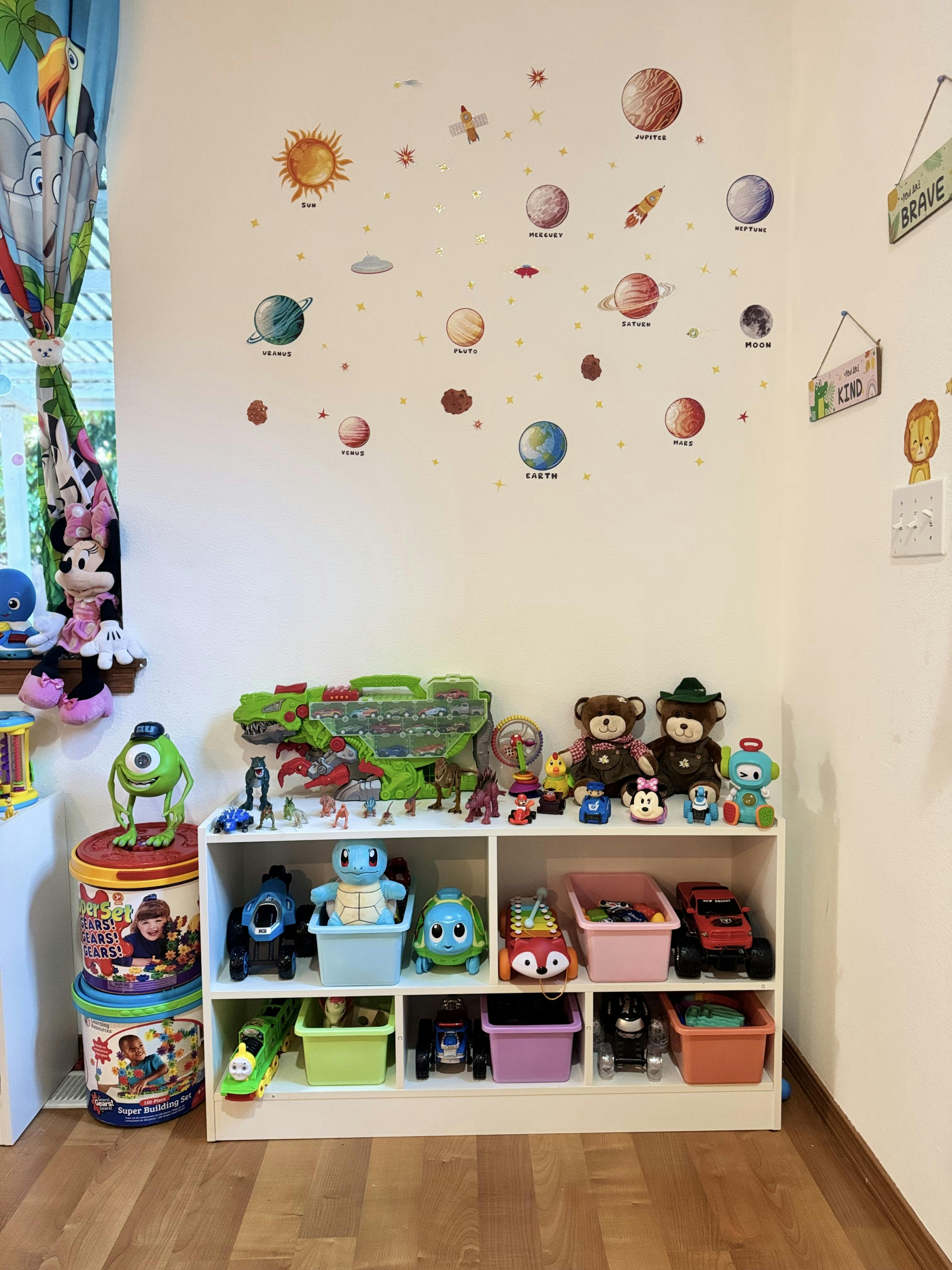 Wall with solar system decals above a white shelf filled with toys