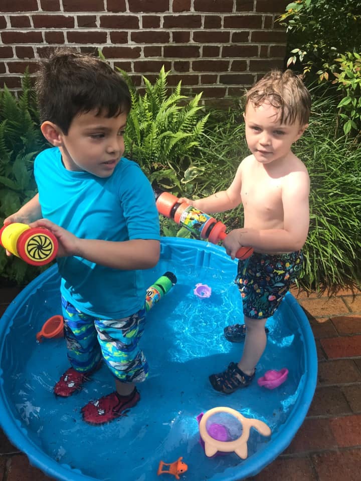 Two children playing in a blue wading pool with water toys
