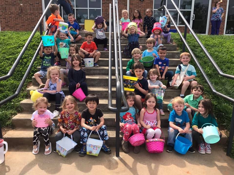 Many children sitting on outdoor stairs holding buckets