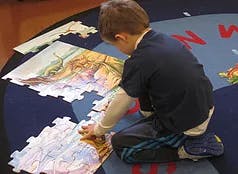 Child kneeling and working on a large floor puzzle
