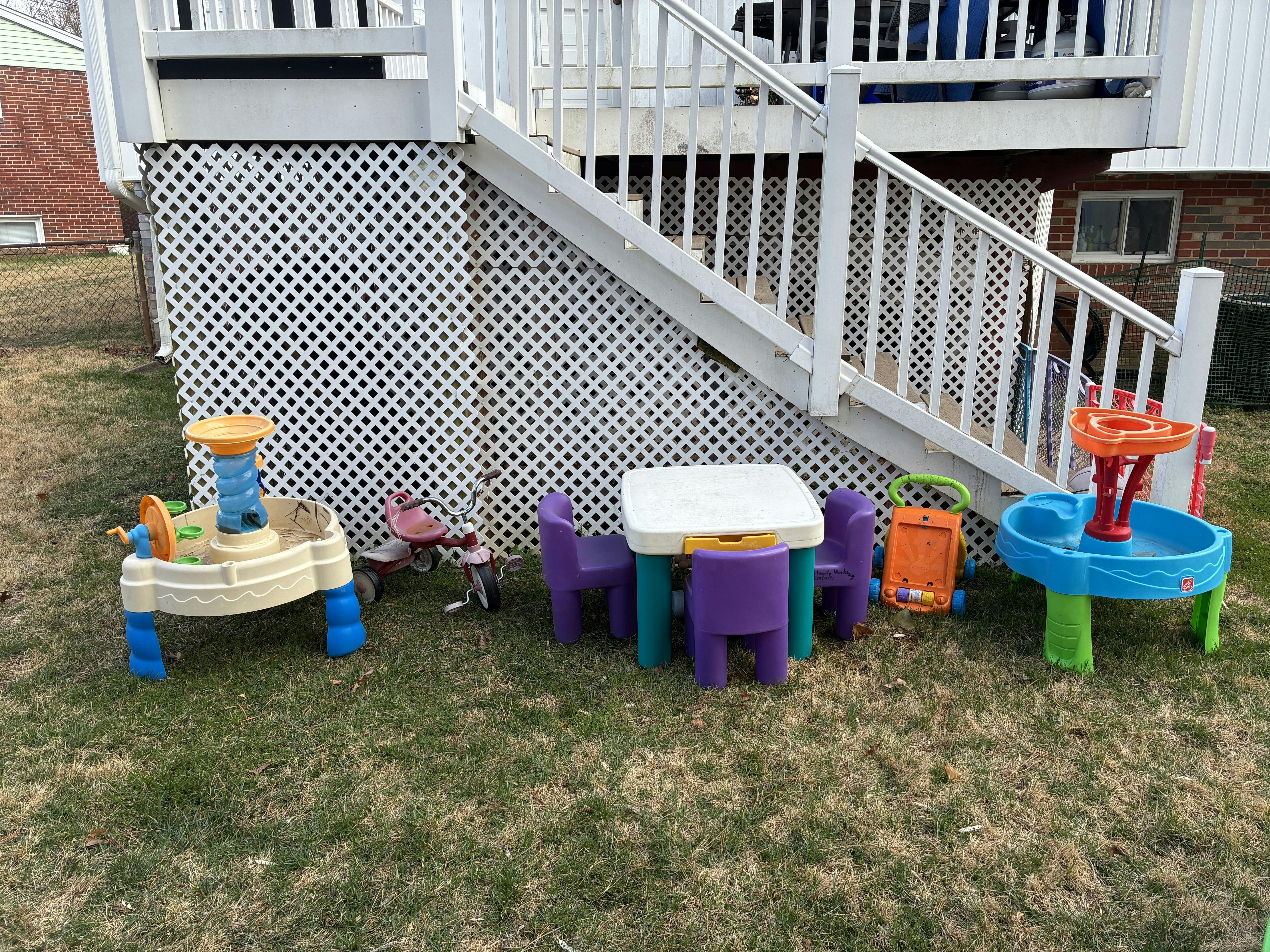 Colorful plastic children's toys and furniture on grass beneath a deck