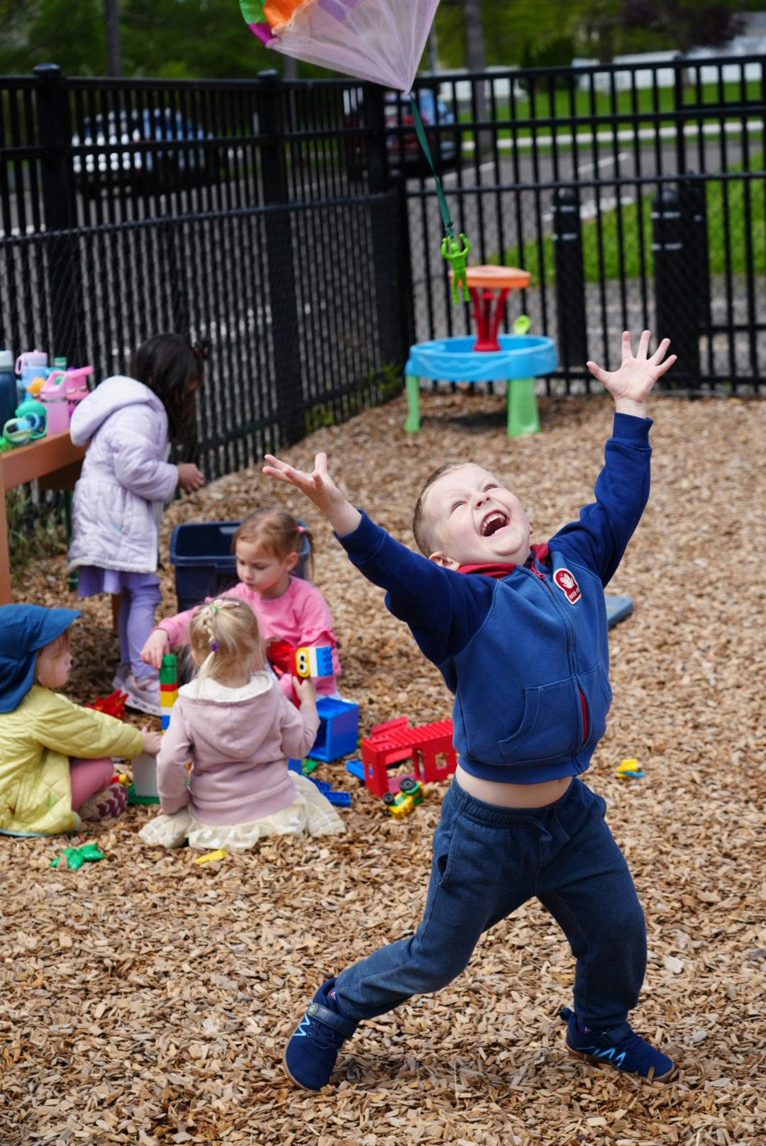 Child smiling with open mouth, arms outstretched, on a wood chip playground