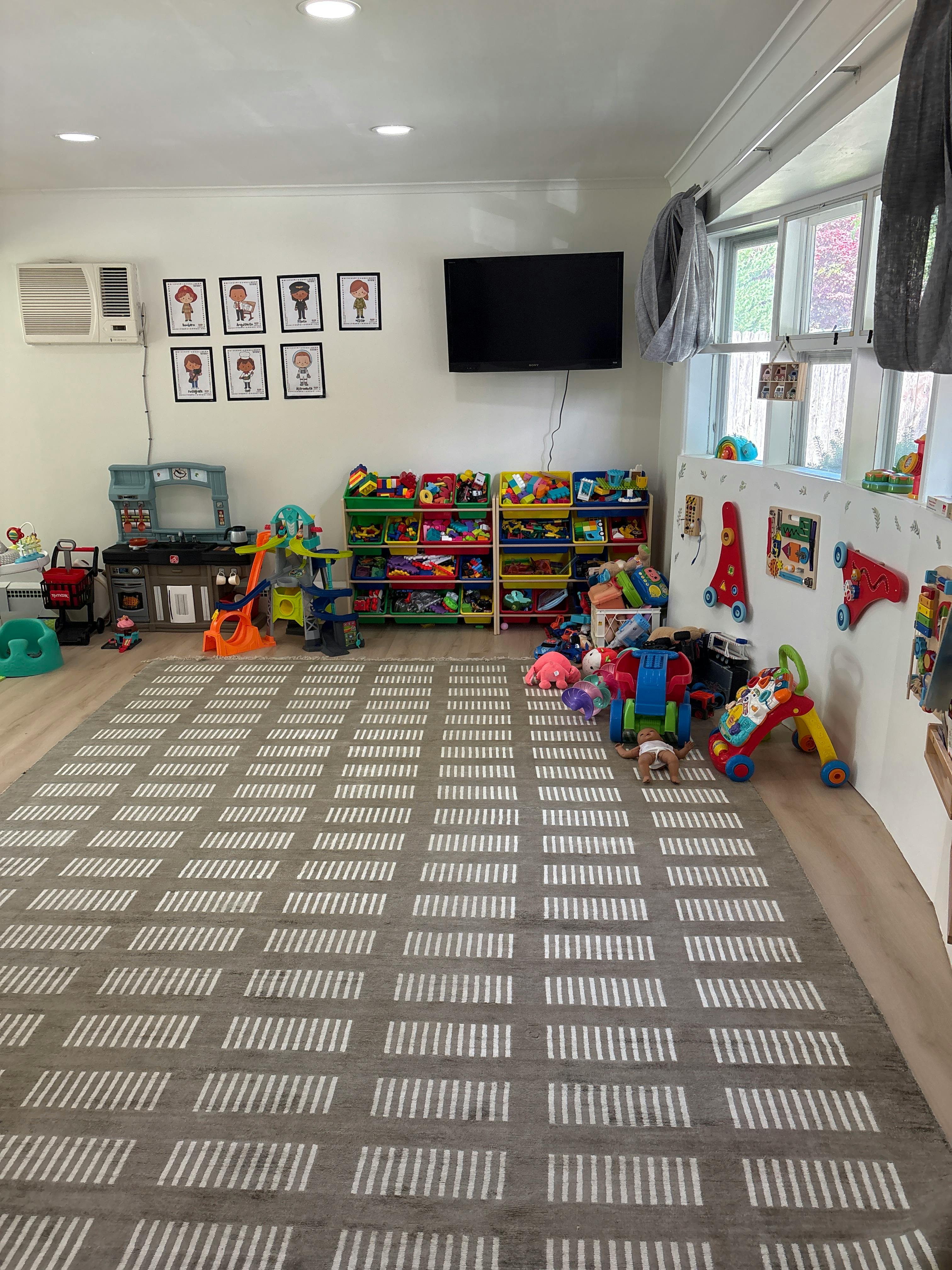 Child crawling on a patterned rug in a brightly lit playroom filled with toys