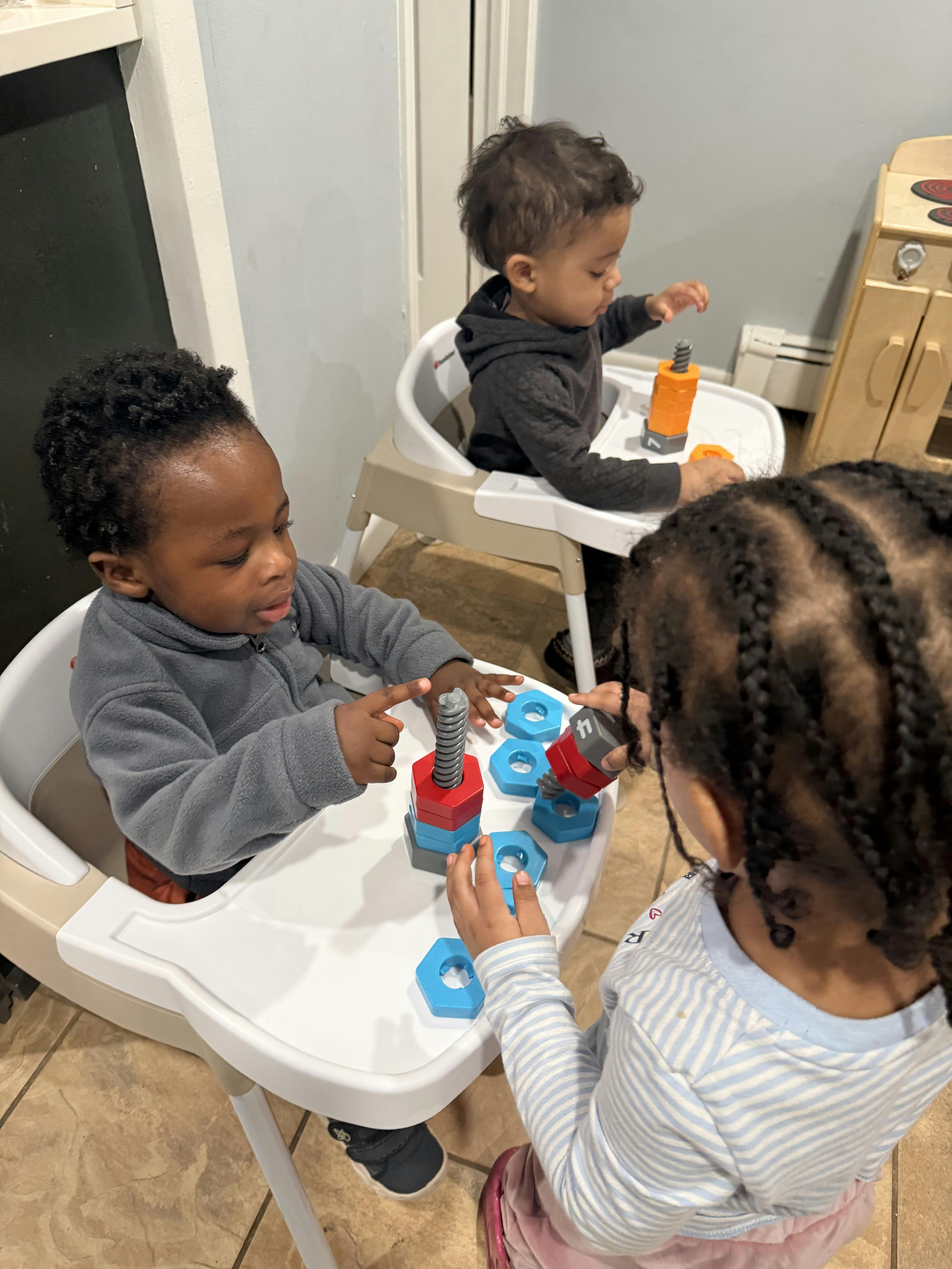 Three children playing with plastic building toys at high chairs