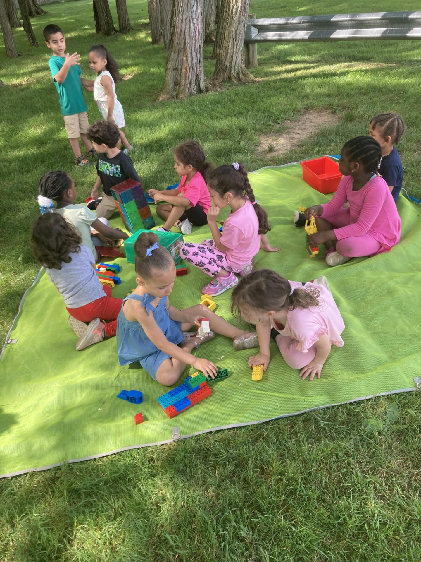 Children playing with toys on a green blanket outdoors