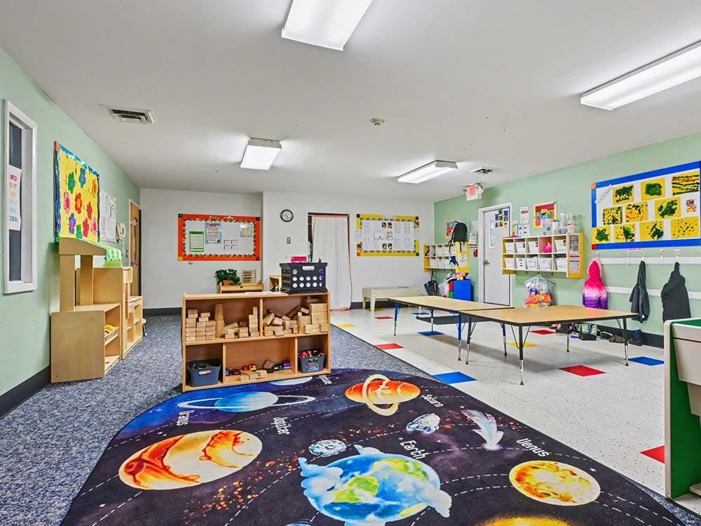 Children's classroom with a planets rug, wooden block shelves, and tables