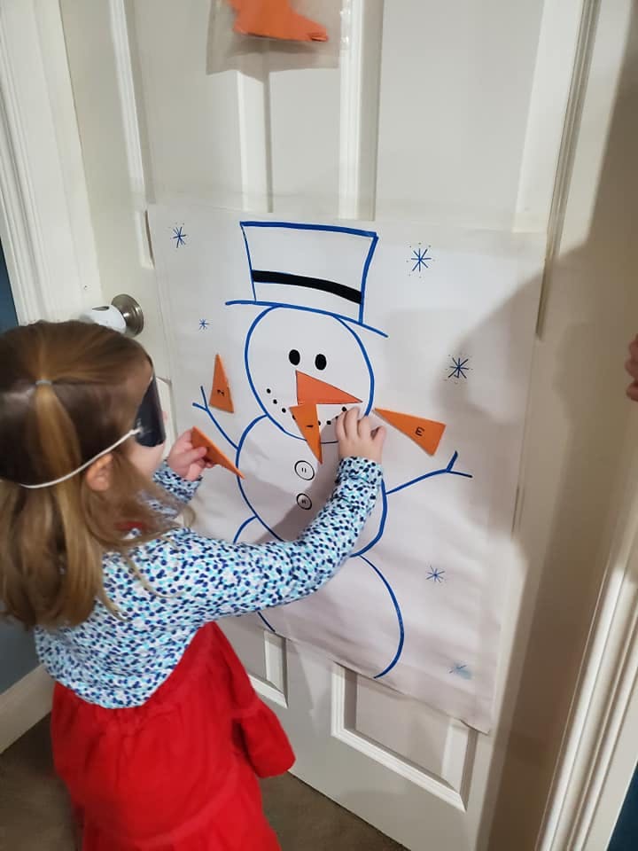 Child with blindfold playing pin the nose on the snowman