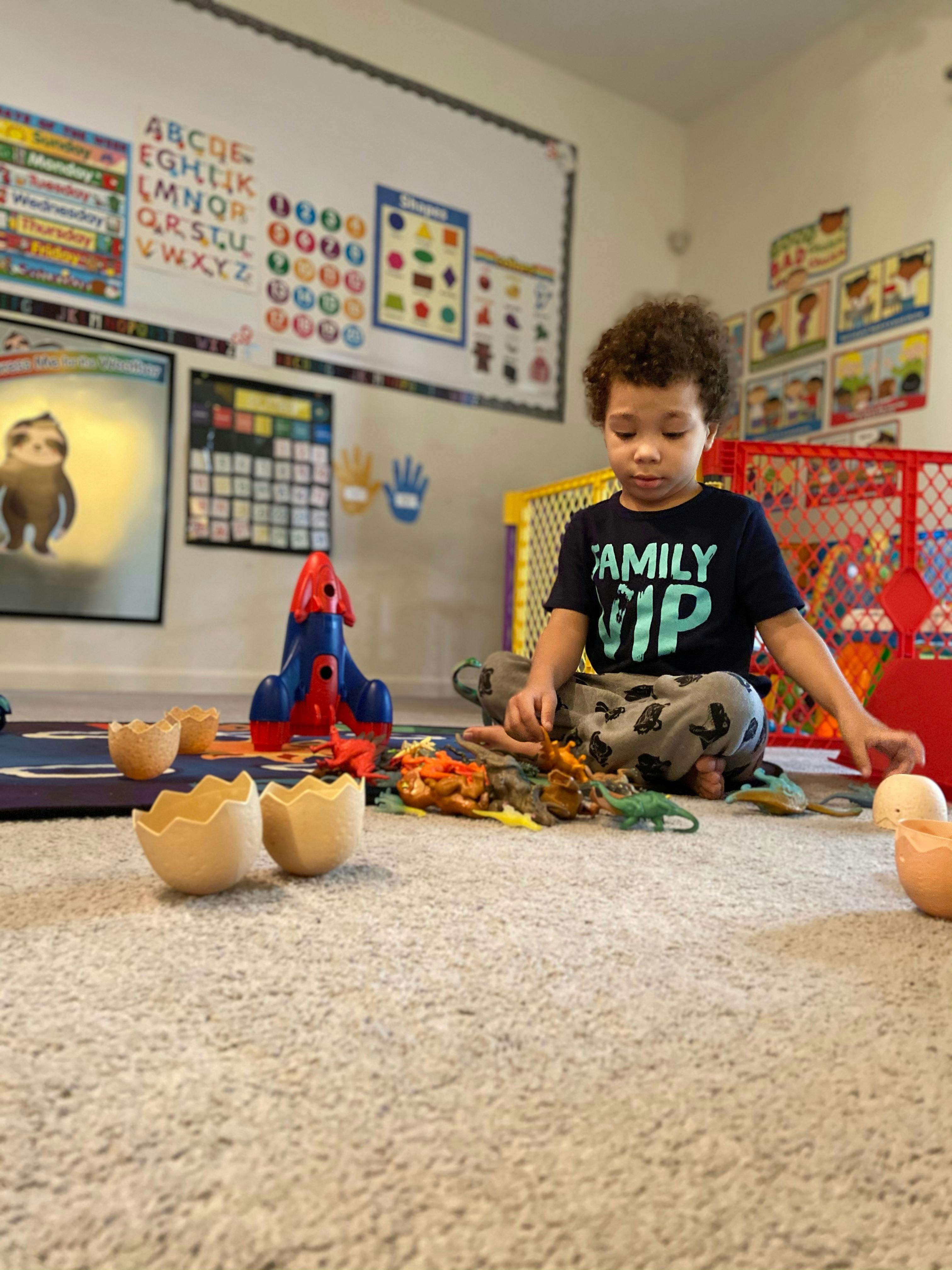 Child sitting on floor playing with toy dinosaurs and rocket