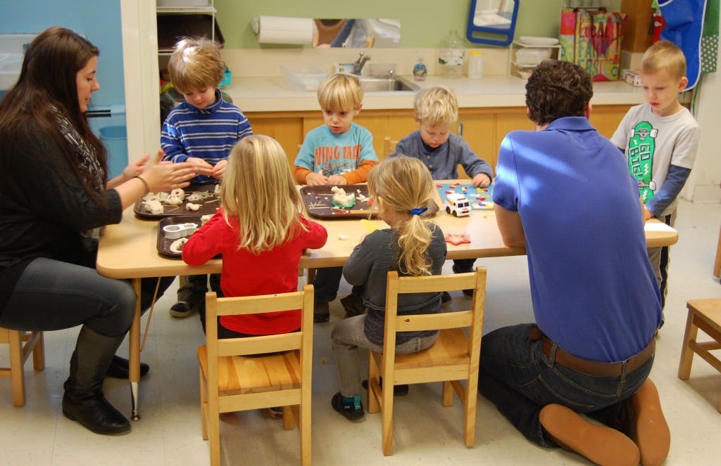 Adults and children sitting at a table with trays of items