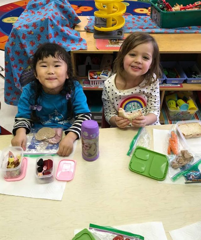 Two children sitting at a table with food containers of food containers