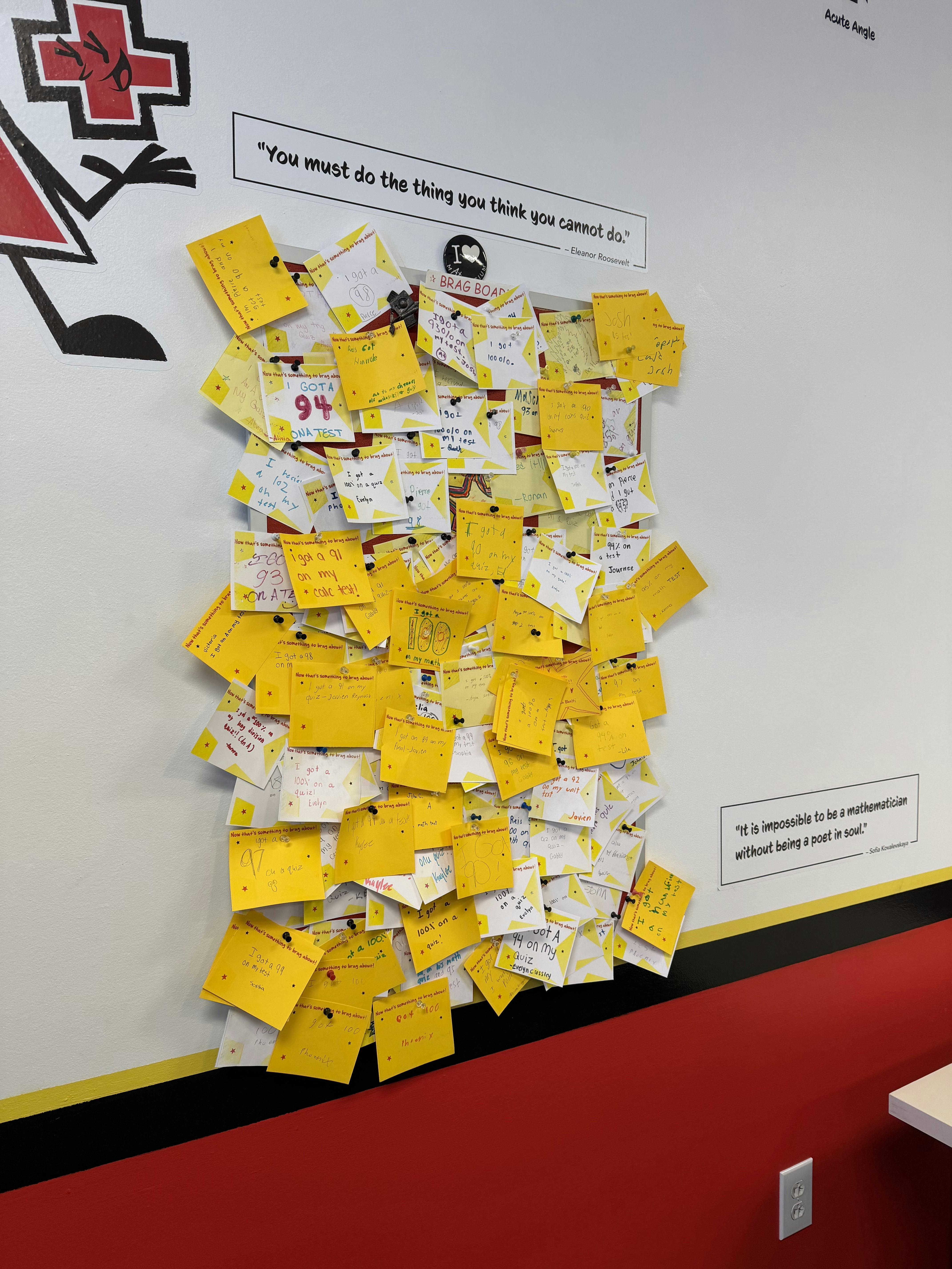 A wall covered in yellow sticky notes with handwritten math scores and positive messages