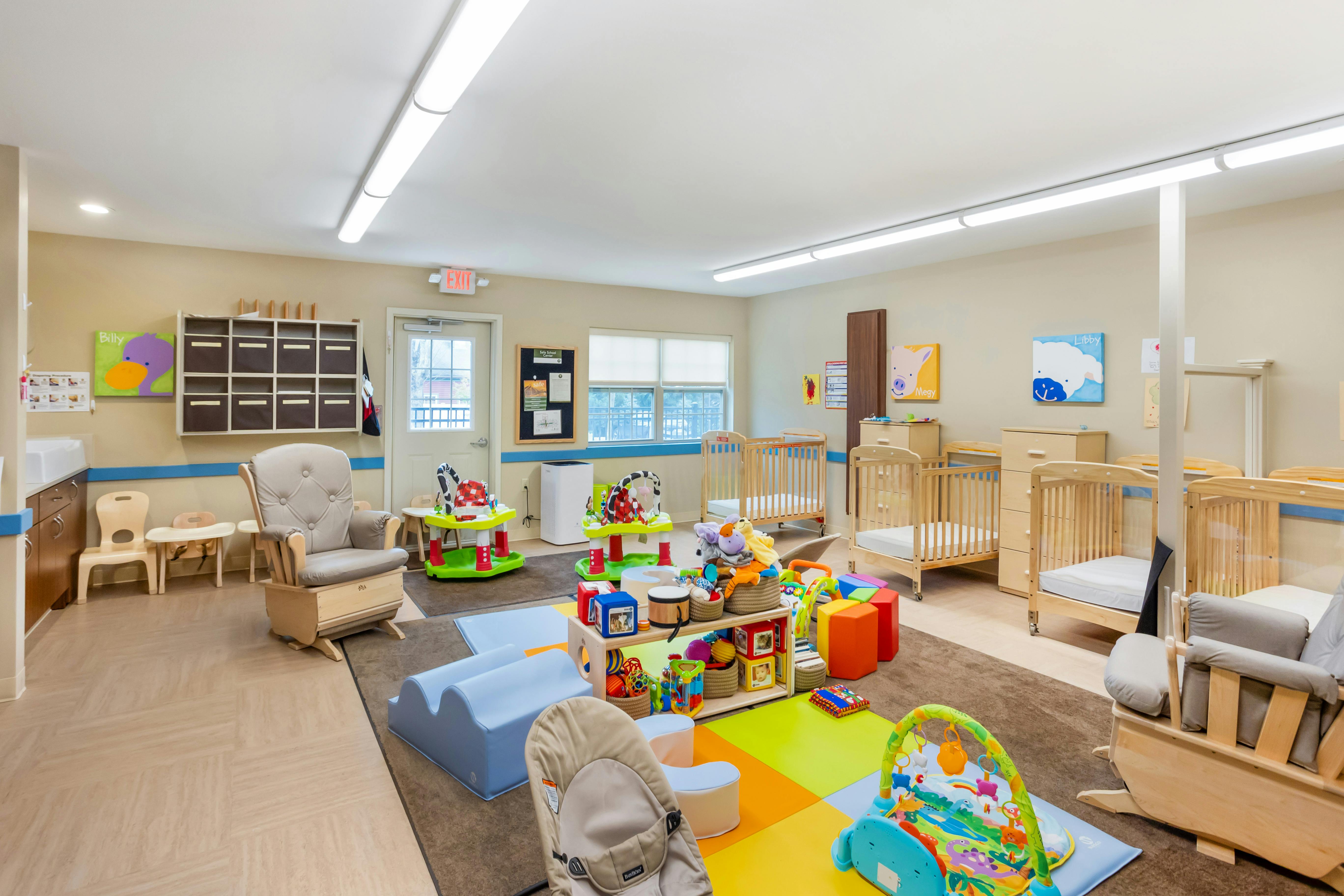 A brightly lit nursery with multiple cribs, rockers, and various colorful play items