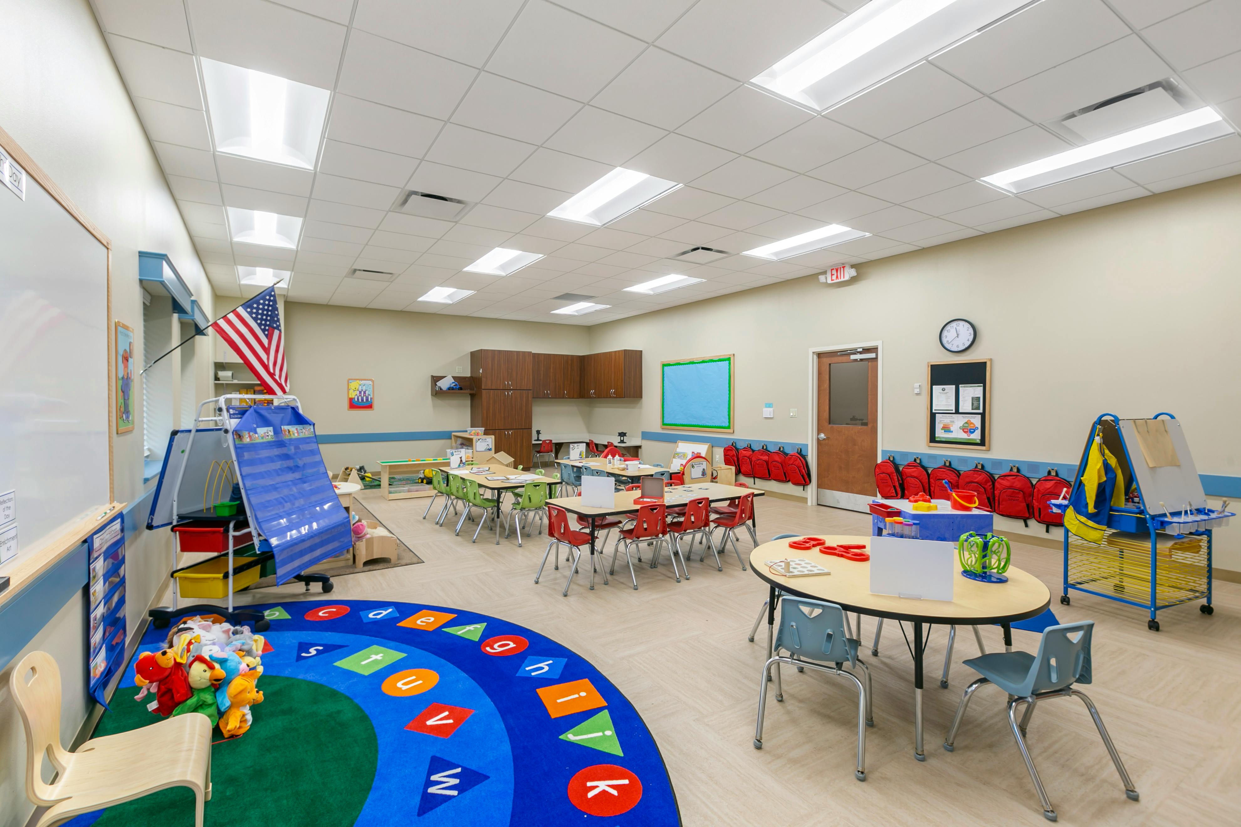 An empty early childhood classroom with colorful carpets, tables, and chairs