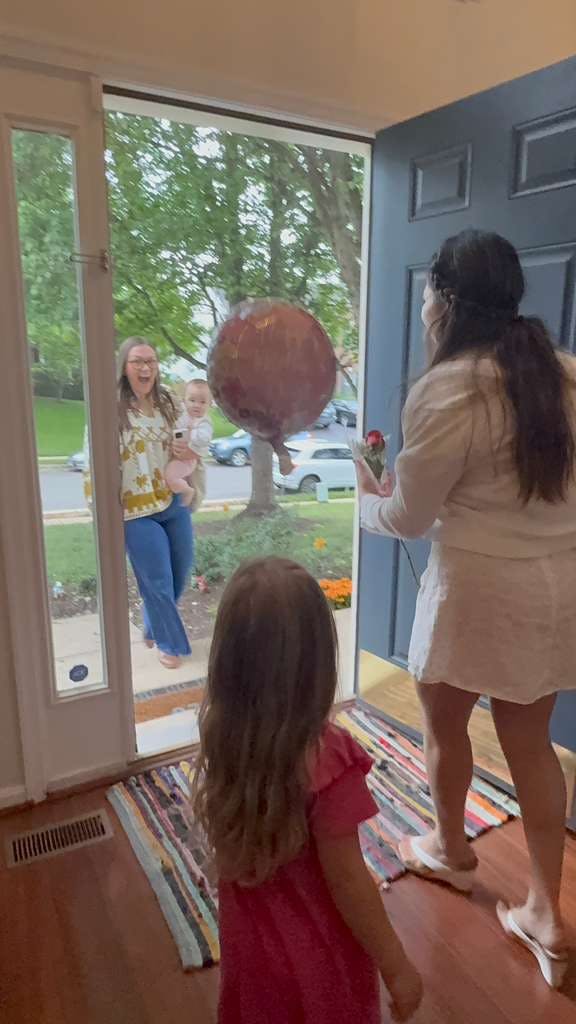 Person holding a child and a large balloon greeting someone at a doorway