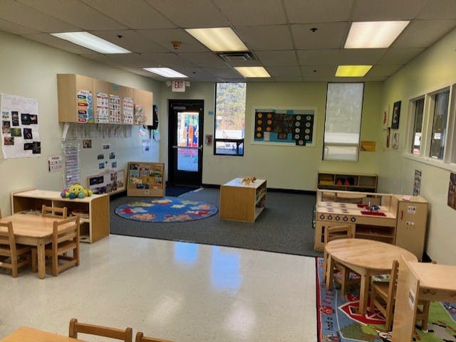 Empty classroom with small tables and chairs, shelves, and a play kitchen