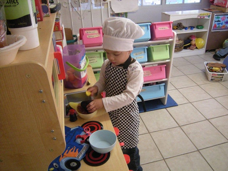 Child in chef hat and apron playing with toy kitchen