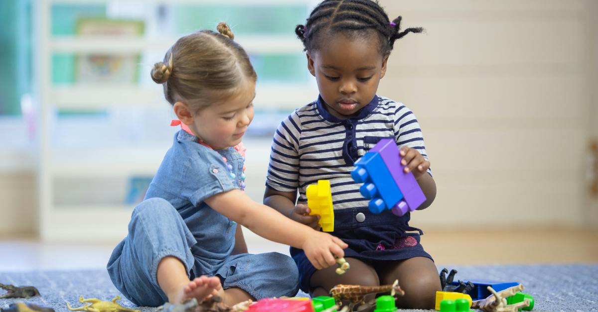 Two children playing with building blocks and toy animals on a rug