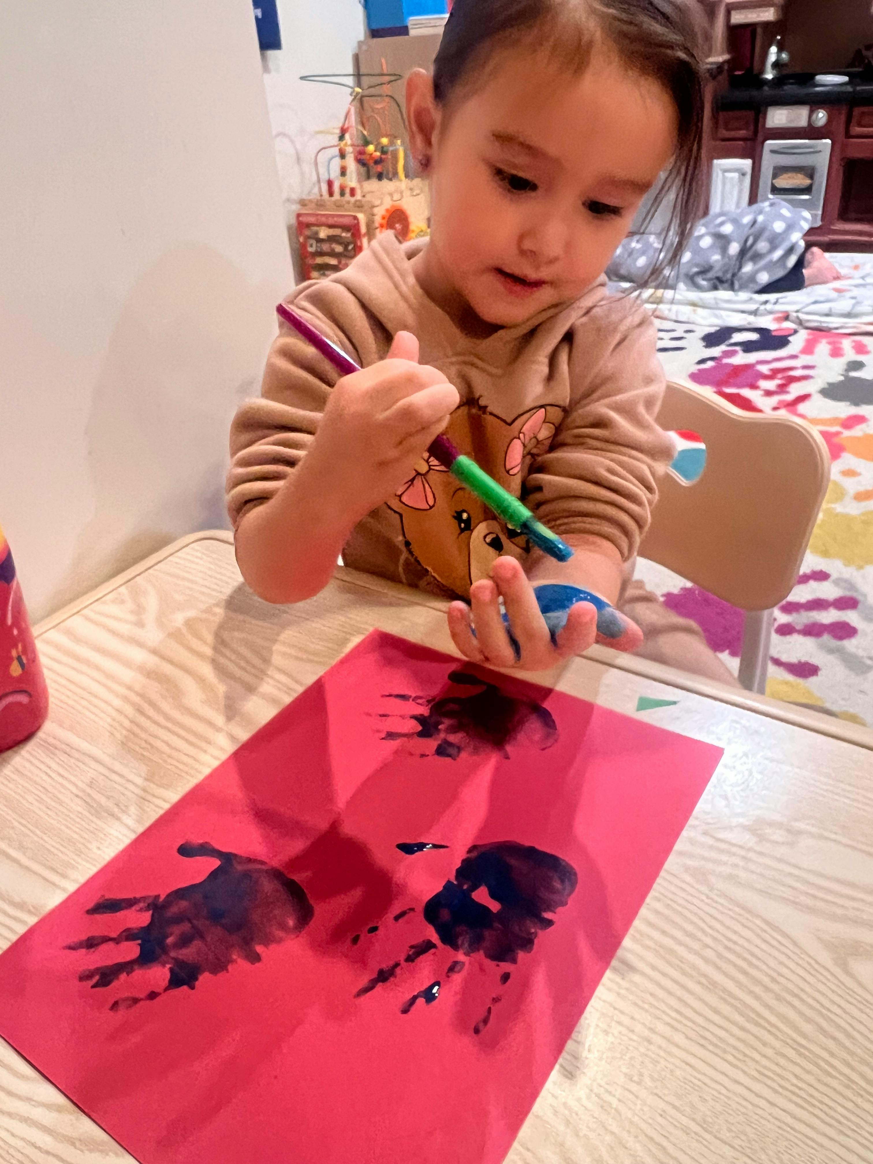 Child making handprints on red paper