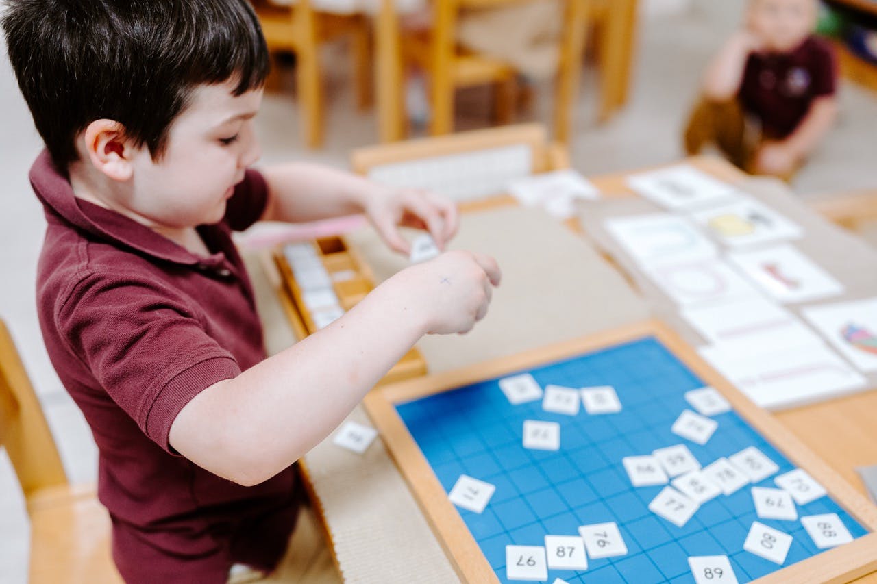 Child playing with small tiles on a blue board at a table