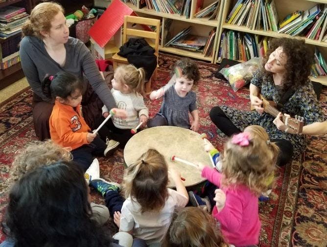 Two people and multiple children playing instruments in a classroom