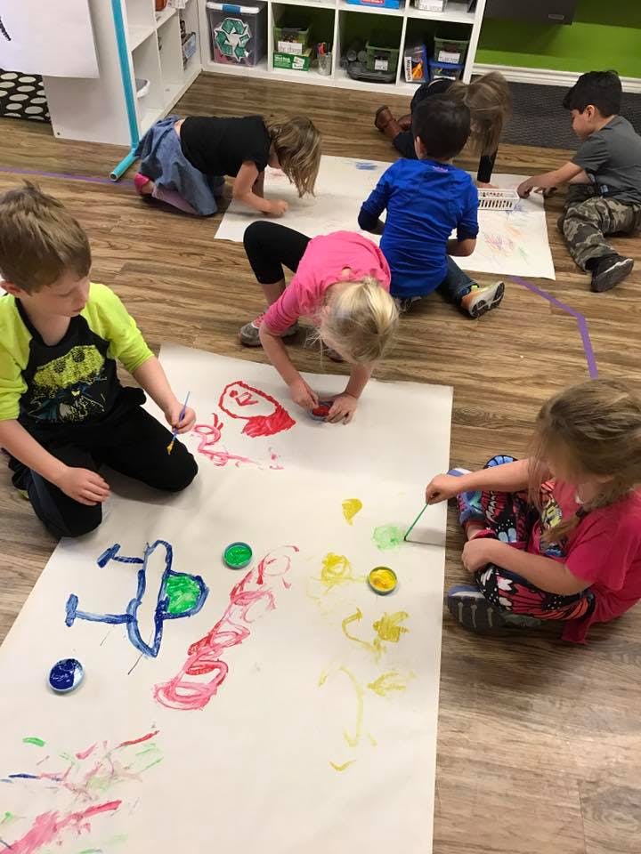 Children painting on large sheets of paper on the floor