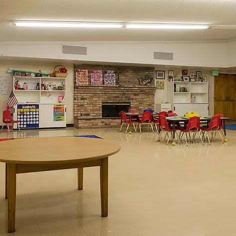 Classroom with small tables and chairs, shelves, and a brick fireplace