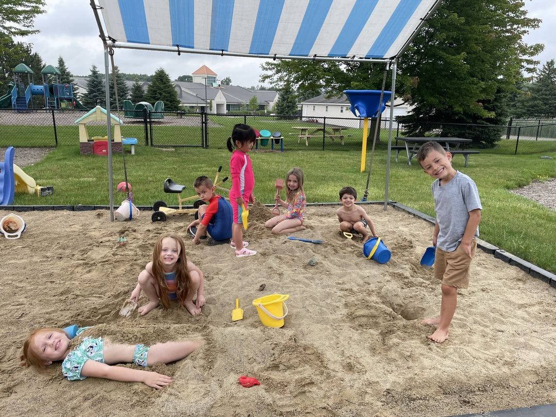 Children playing in a large sandbox with toys