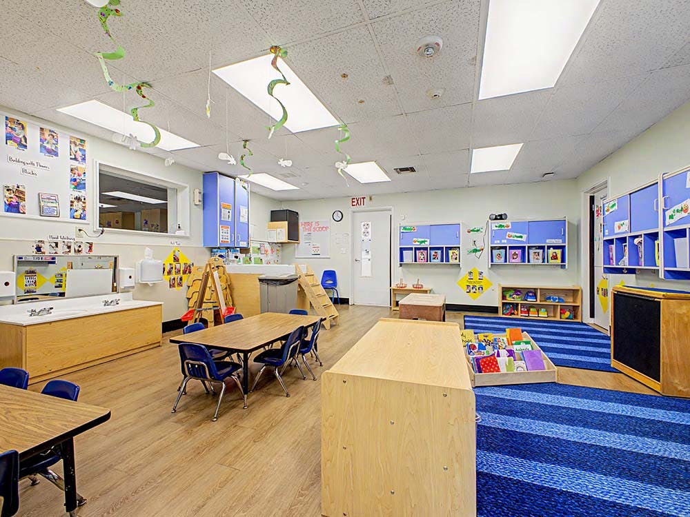Empty classroom with small tables, chairs, cabinets, and a sink area