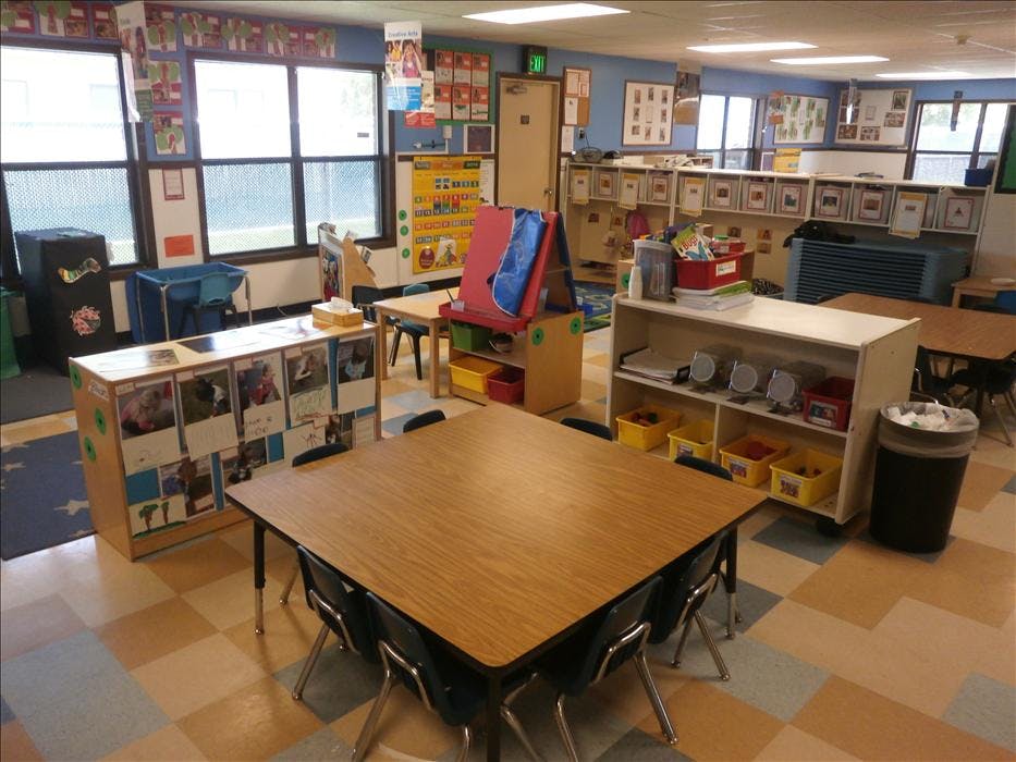 Classroom with tables, chairs, windows, and shelving with learning materials