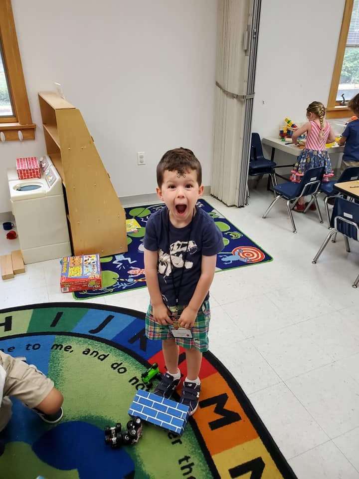 Child standing on a rug with mouth open in a classroom