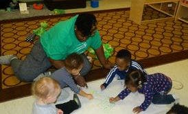 Adult and three children drawing on paper on the floor