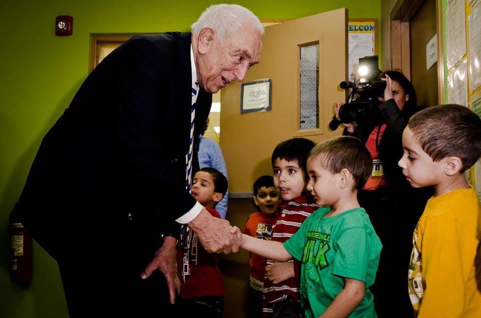 Older person in suit shaking hands with a child in a classroom