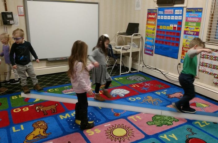 Children walking on a white line on a colorful alphabet rug